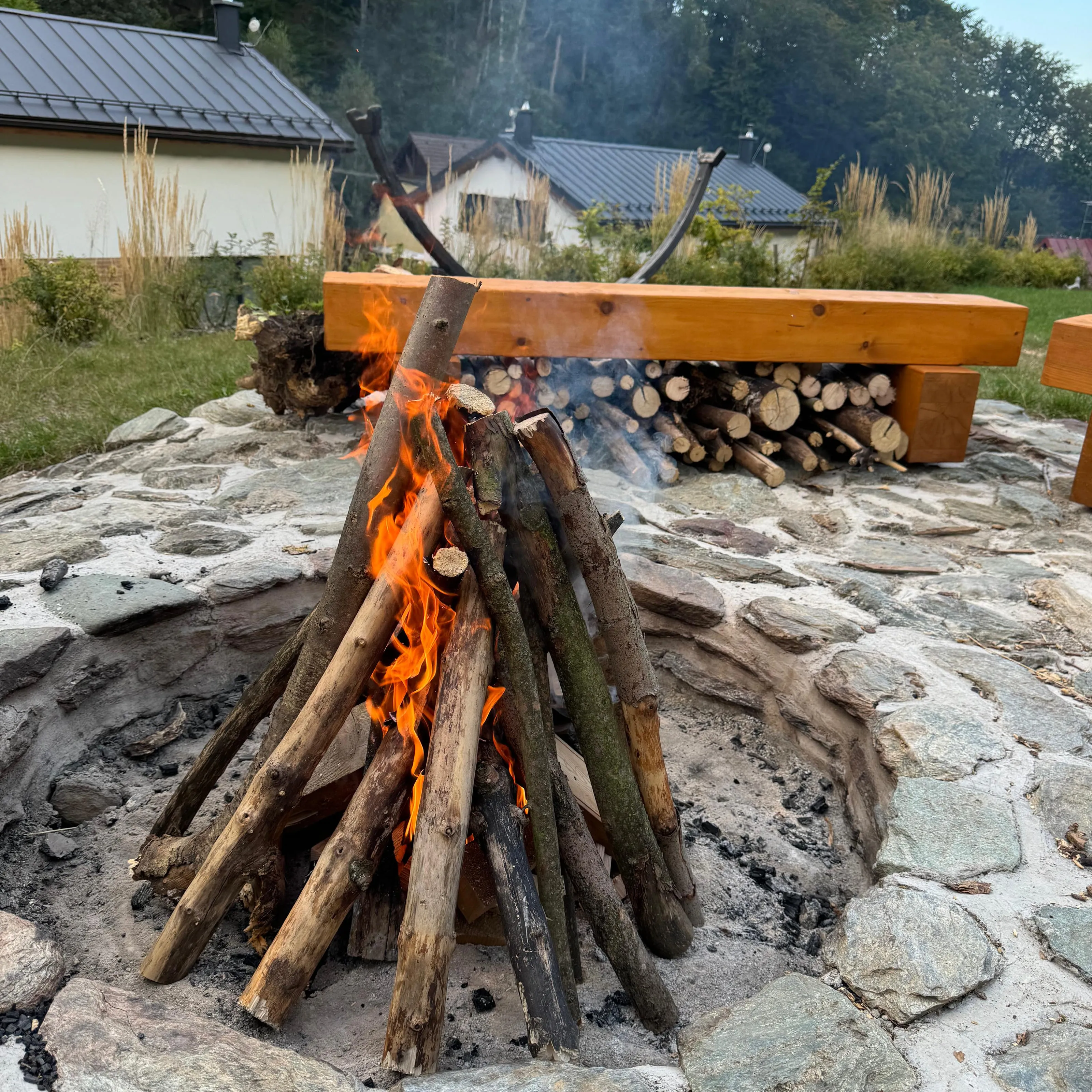 A fire in the stone fire pit in the garden, wooden bench behind